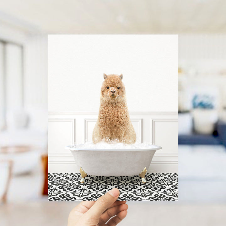 A fluffy brown alpaca sitting in a white bathtub filled with bubbles, with a hand holding the photo up to the viewer.