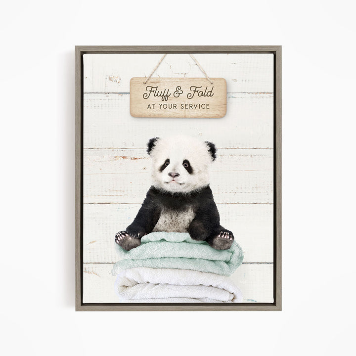 A panda bear sitting on a stack of towels, with a wooden sign above that says "Fuffy & Fold at your service".