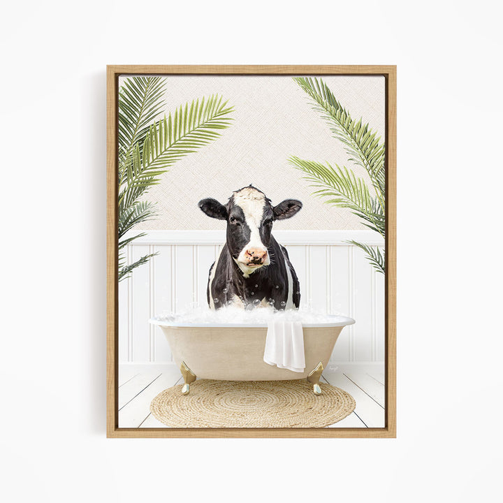 A black and white cow is sitting in a white bathtub filled with water, surrounded by green palm leaves.