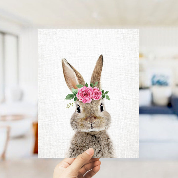 A hand is holding up a framed image of a rabbit wearing a pink flower crown.
