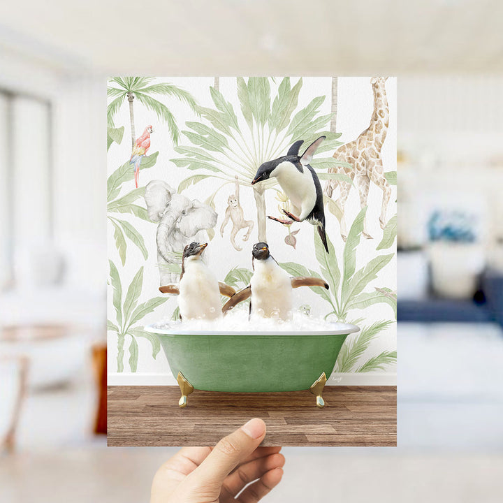 A hand holds up a framed image depicting two penguins sitting in a bathtub, surrounded by a tropical jungle scene with various animals.