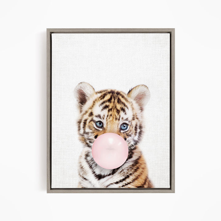 A young tiger cub blowing a bubble with a pink bubble gum bubble.