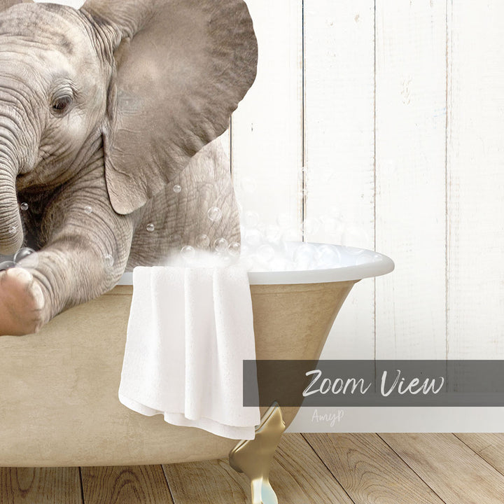 A baby elephant sitting in a bathtub filled with water, surrounded by bubbles, with a towel and wooden floor in the background.