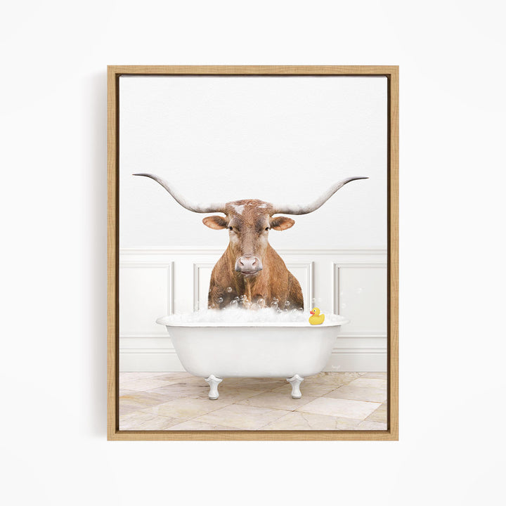 A brown steer with long horns is sitting in a white bathtub, with a yellow rubber duck floating in the water.