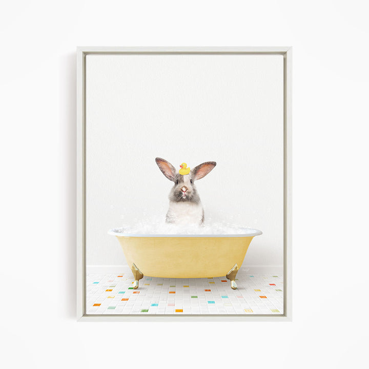 A gray and white rabbit sitting in a yellow bathtub filled with bubbles, with a yellow rubber duck floating on the water.