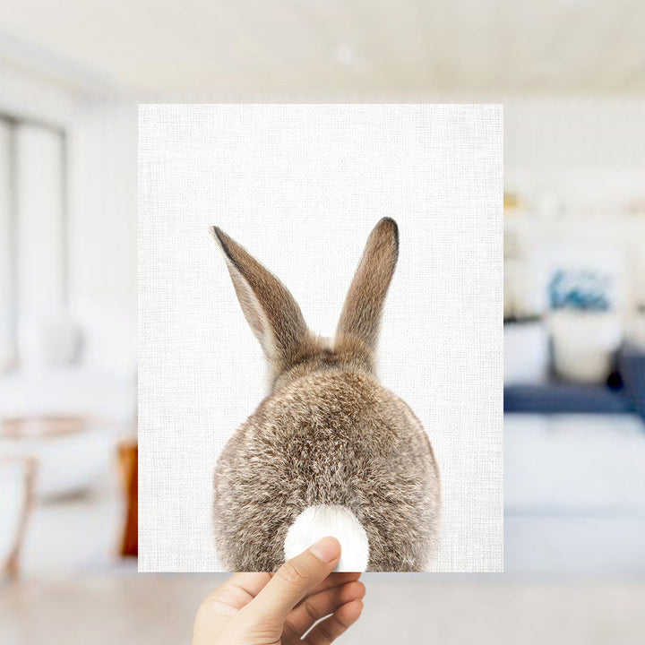A hand is holding up a picture of a rabbit's back, showing its fluffy tail.