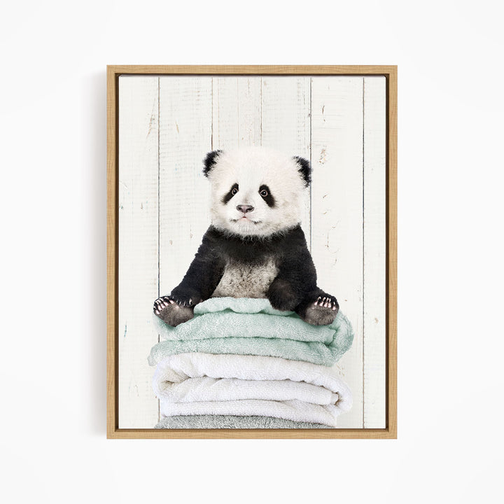 A panda bear sitting on a stack of towels, with a white background and a wooden frame.