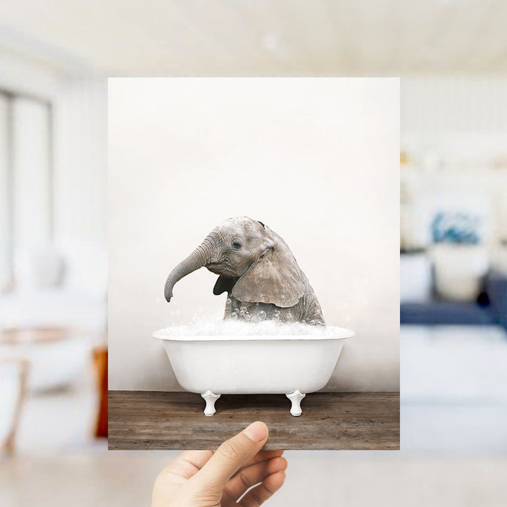 A baby elephant sitting in a white bathtub filled with water, with a blurred background suggesting a bathroom setting.