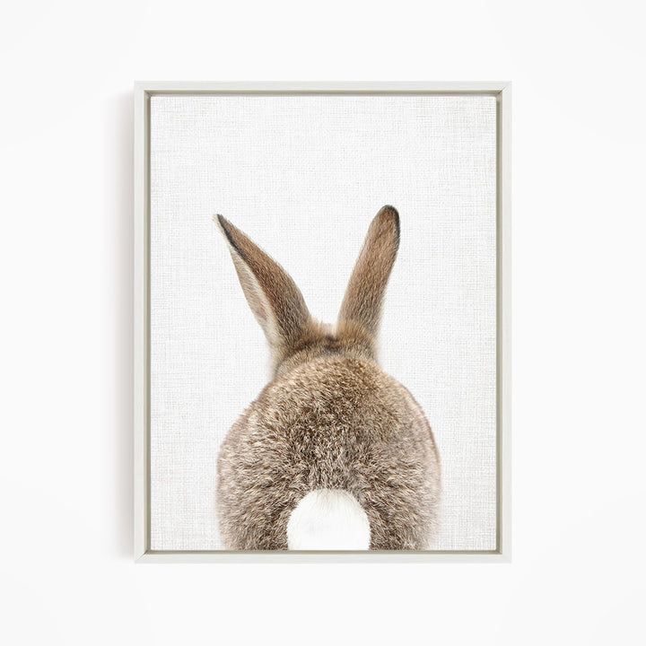 A close-up of a rabbit's back, showing its fluffy tail and long ears, is the focus of the image.
