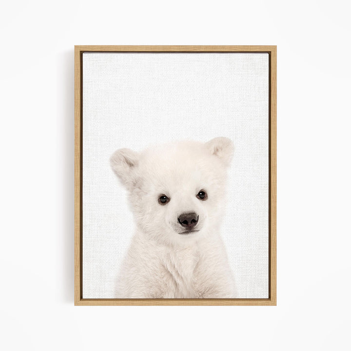 A cute white polar bear cub is the focus of the image, captured in a close-up portrait.