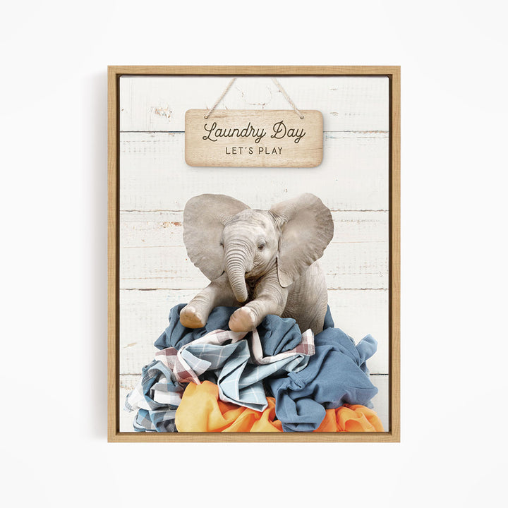 A framed image of a baby elephant sitting atop a pile of laundry, with a sign above that says "Laundry Day Let's Play".