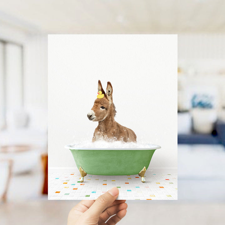A donkey is sitting in a green bathtub filled with bubbles, with a yellow rubber duck floating on its head.
