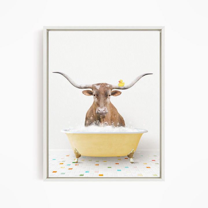 A brown cow with long horns is sitting in a yellow bathtub filled with bubbles, with a yellow rubber duck perched on its head.