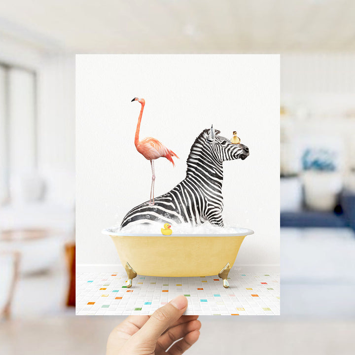 A hand holds up a collage of two images: a zebra standing in a bathtub with a pink flamingo, and a yellow bathtub with a rubber duck.