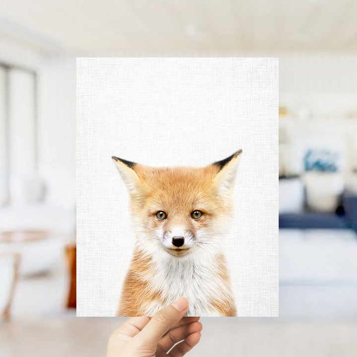 A hand is holding up a framed print of a close-up portrait of a fox, with a blurred background suggesting an indoor setting.