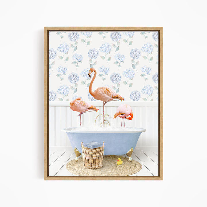 A framed image depicting three flamingos standing in a blue bathtub filled with water, surrounded by a wicker basket and yellow rubber ducks.