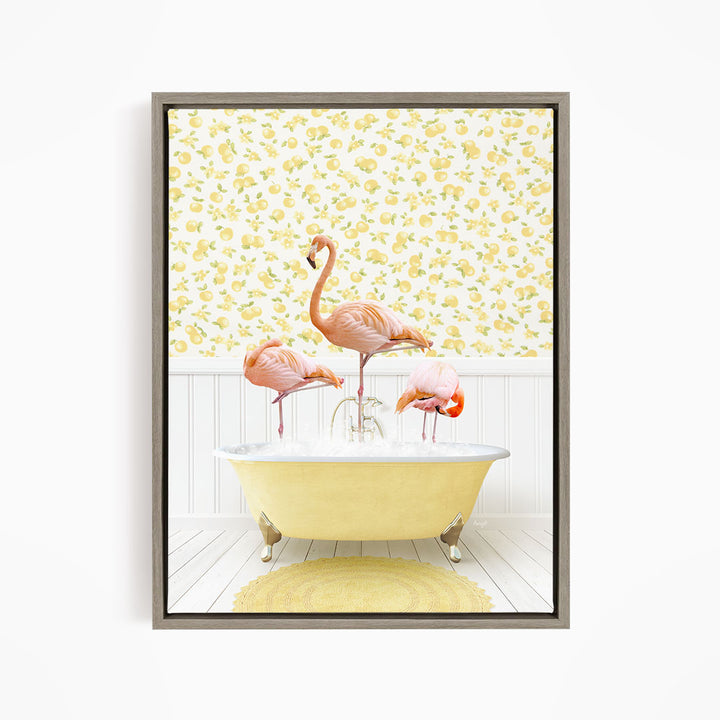 A framed image depicting three pink flamingos standing in a yellow bathtub, with a yellow and white floral wallpaper in the background.