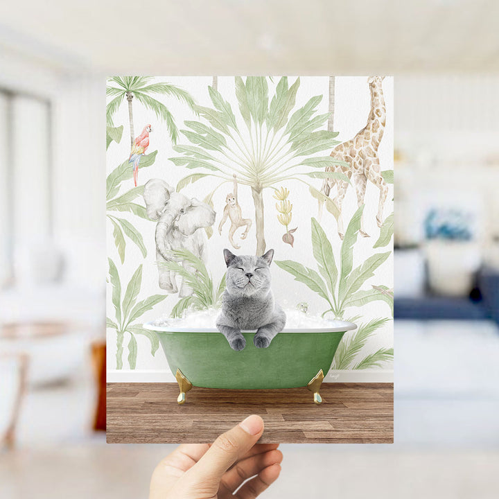 A hand holds up a collage of an illustration featuring a gray cat sitting in a green bathtub surrounded by various animals, including a giraffe, elephant, and parrot, against a tropical background.