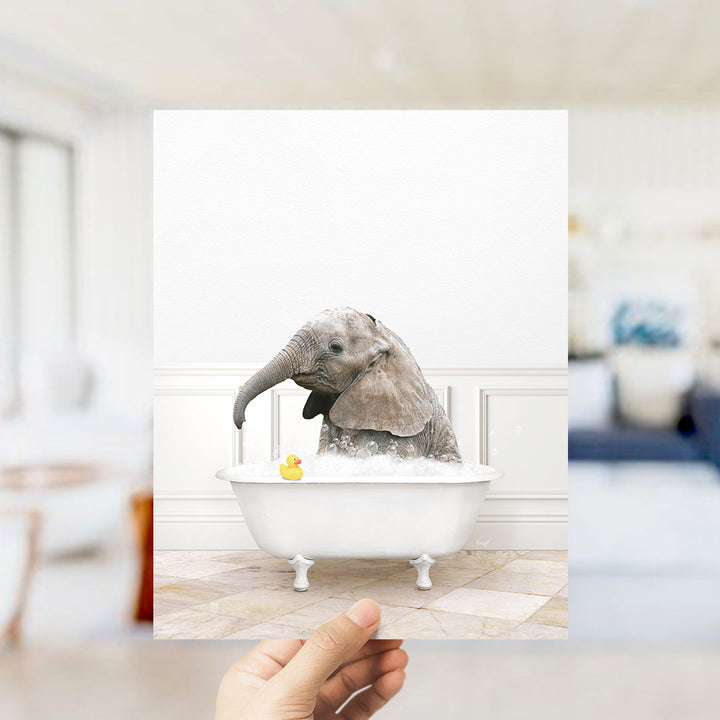 A small gray elephant is sitting in a white bathtub filled with water, with a yellow rubber duck floating nearby.