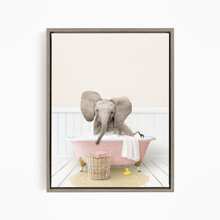 A gray elephant is sitting in a pink bathtub filled with water, surrounded by a yellow rubber duck and a basket of bath toys.