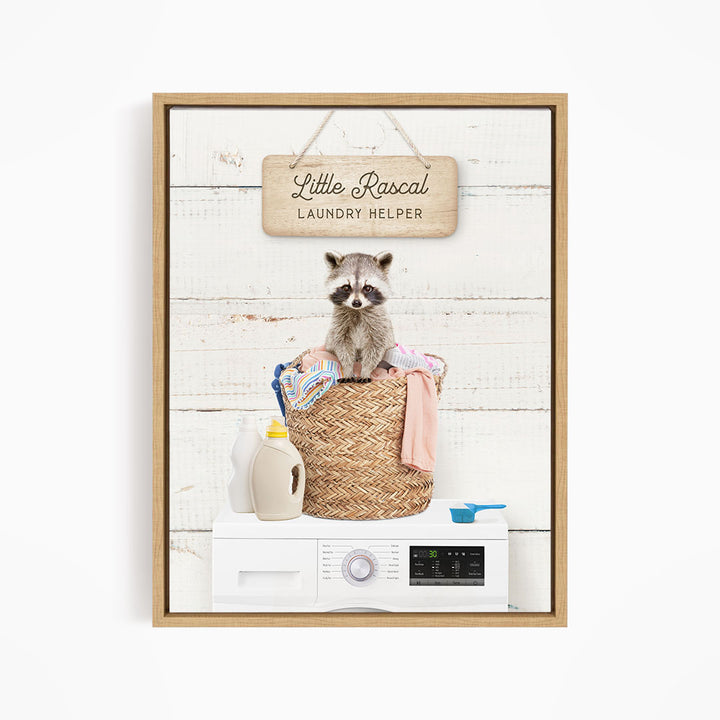 A raccoon sitting in a woven laundry basket, with a sign that reads "Little Racal Laundry Helper" above it.