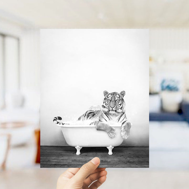 A black and white photograph of a tiger sitting in a bathtub, with a blurred background suggesting an indoor setting.