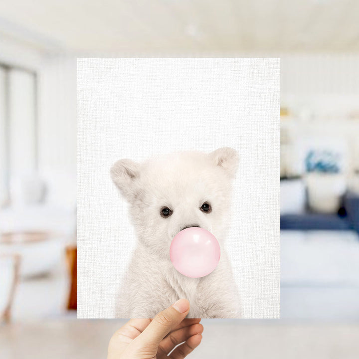 A hand is holding up a white polar bear with its mouth on a pink bubblegum bubble.