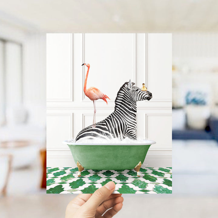 A hand holds up a framed image depicting a zebra sitting in a green bathtub, with a pink flamingo standing on its back.