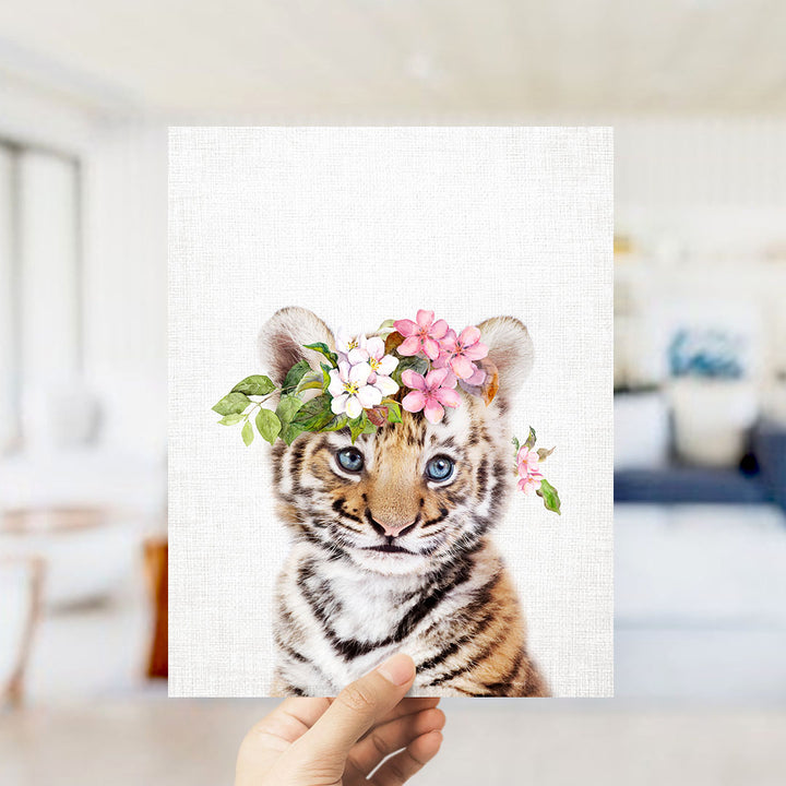 A hand is holding up a framed photograph of a tiger cub with a floral headpiece.