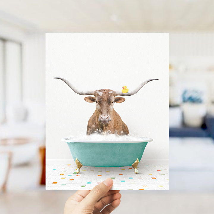 A brown cow with long horns is sitting in a green bathtub filled with bubbles, with a yellow rubber duck floating on its head.