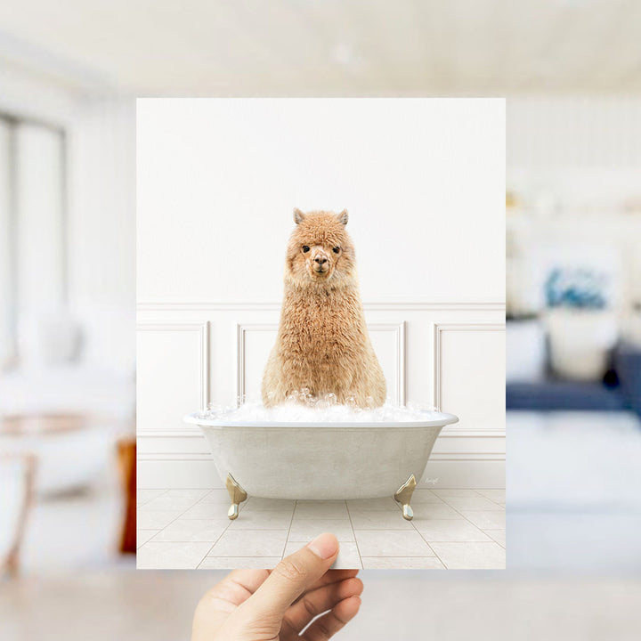 A fluffy brown alpaca sitting in a white bathtub filled with bubbles, with a blurred background suggesting a bathroom setting.
