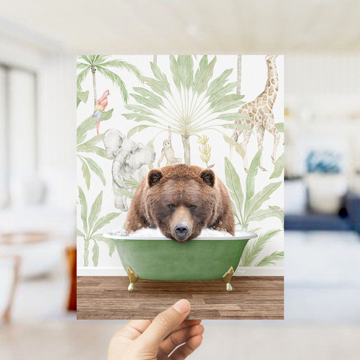 A hand holds up a framed image depicting a brown bear sitting in a green bathtub, surrounded by tropical foliage and animals.