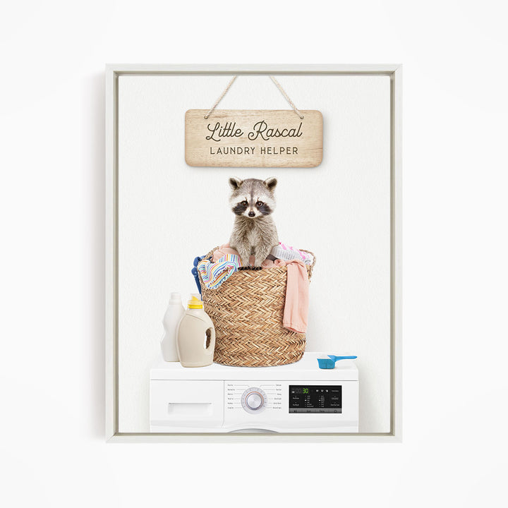 A raccoon sitting in a woven laundry basket, with a sign that reads "Little Racal Laundry Helper" above it.