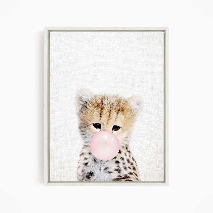 A young cheetah with spotted fur blowing a bubble with a pink bubble gum bubble.