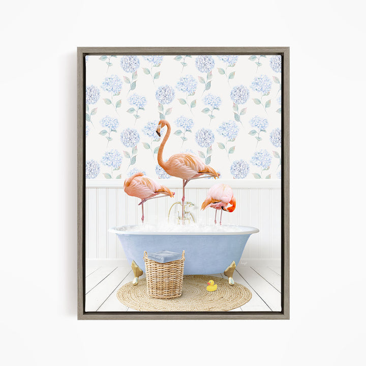 A framed image depicting three pink flamingos standing in a blue bathtub filled with water, surrounded by a wicker basket and yellow rubber ducks.