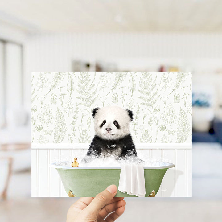 A hand holding a framed print of a panda bear sitting in a bathtub filled with bubbles, surrounded by a green and white floral pattern.