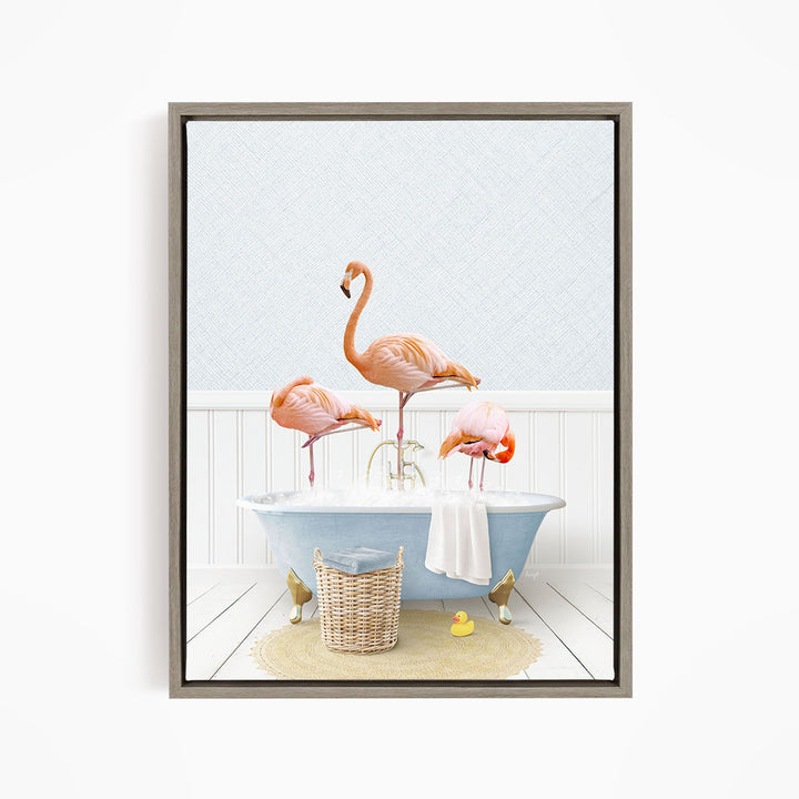 A framed image depicting three flamingos standing in a bathtub filled with water, surrounded by a basket of bath toys and a towel.