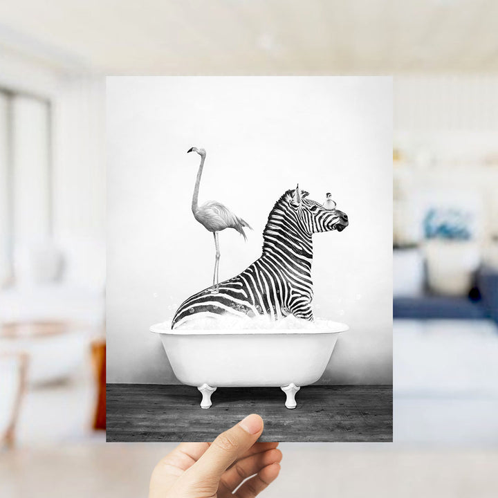 A hand holds up a black and white photograph of a zebra sitting in a bathtub, with a flamingo standing on its back.