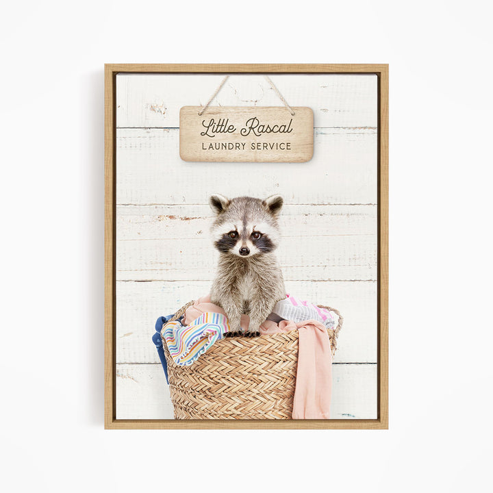 A raccoon sitting in a woven laundry basket, with a sign above that reads "Little Racal Laundry Service".