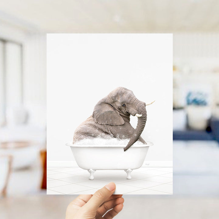 A gray elephant sitting in a white bathtub filled with bubbles, with a blurred background suggesting a bathroom setting.