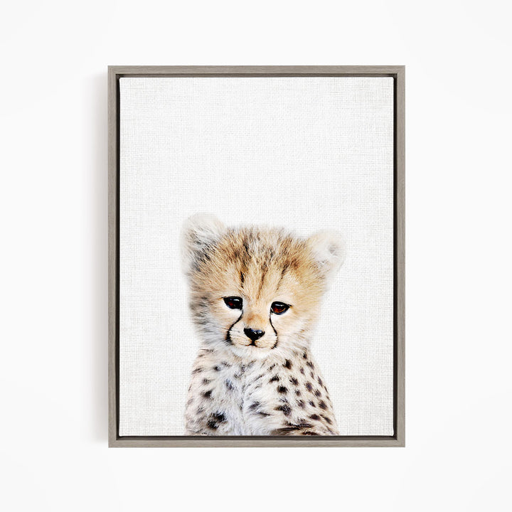 A young cheetah cub with a spotted coat and a curious expression is the focus of the image.