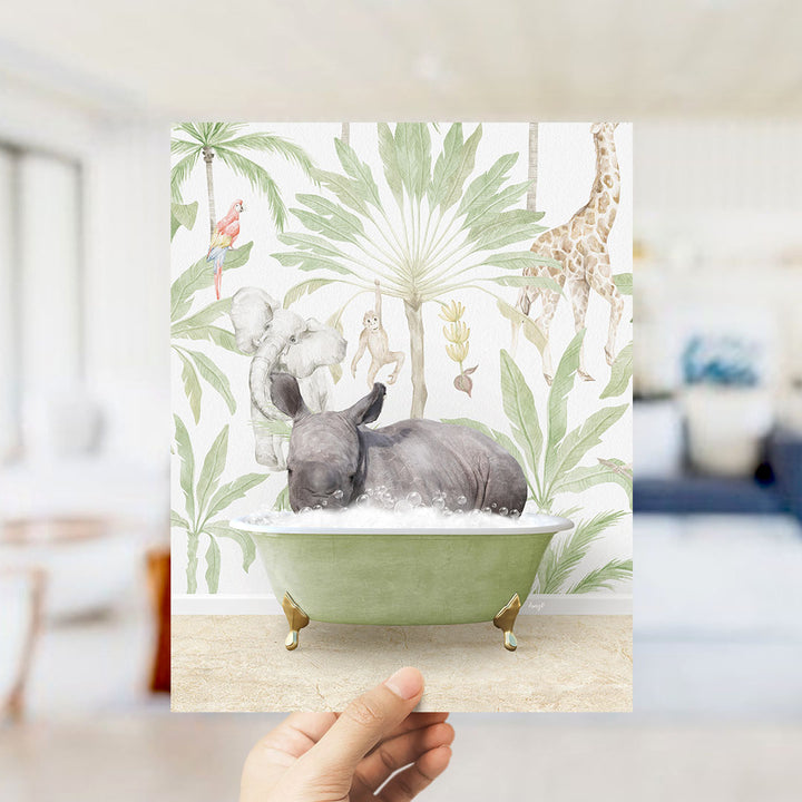 A hand holds up a framed print featuring a whimsical illustration of a rhinoceros bathing in a green bathtub, surrounded by tropical foliage and animals.