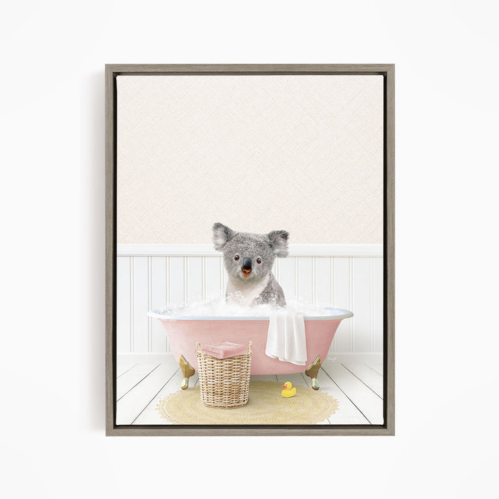 A koala bear sitting in a pink bathtub filled with water, surrounded by a yellow rubber duck and a wicker basket.
