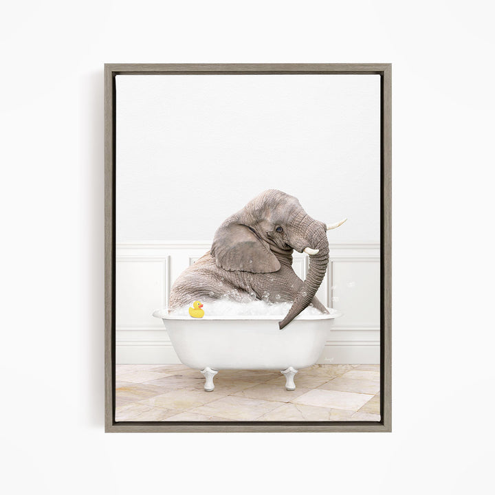 A gray elephant is sitting in a white bathtub filled with water, with a yellow rubber duck floating nearby.