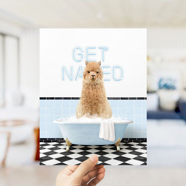 A hand holding a framed image of a brown alpaca sitting in a bathtub, with the words "GET NAKED" written on the wall behind it.