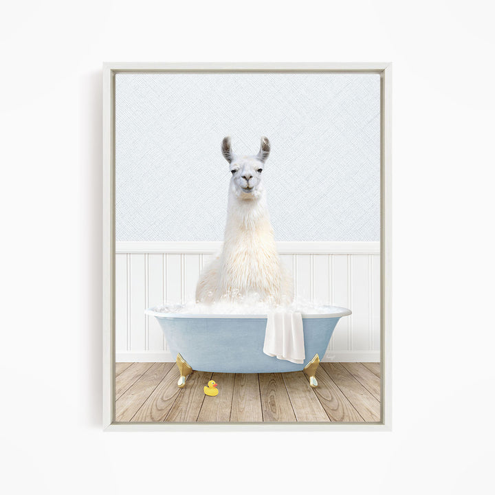 A white llama sitting in a blue bathtub filled with bubbles, with a towel hanging on the side and rubber duckies floating in the water.