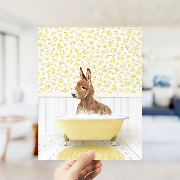 A brown donkey sitting in a yellow bathtub filled with bubbles, surrounded by a yellow and white floral patterned wall.