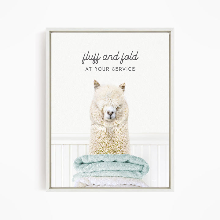 A fluffy alpaca sitting on a stack of light blue towels, with the text "fluff and fold at your service" written above the image.