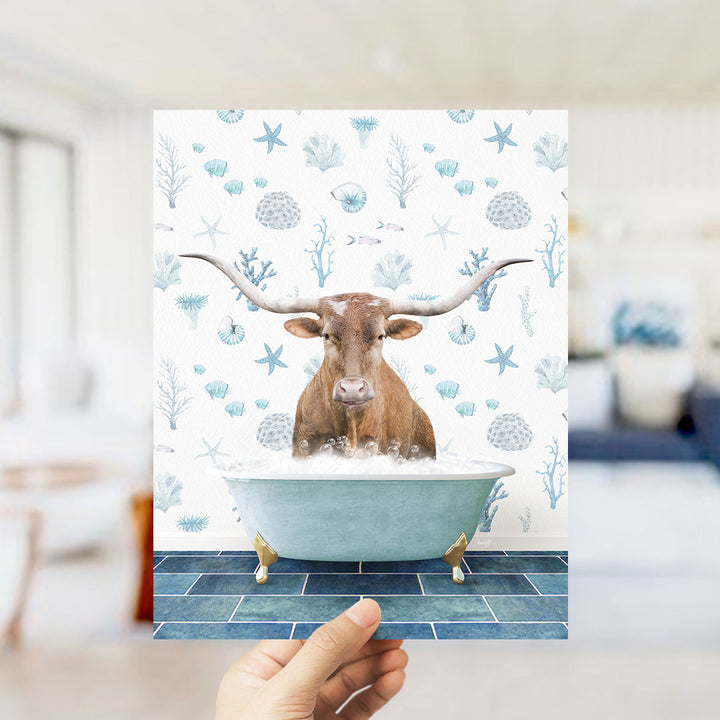 A hand is holding up a print featuring a brown cow with long horns sitting in a blue bathtub filled with bubbles, surrounded by a pattern of seashells, starfish, and other marine life.