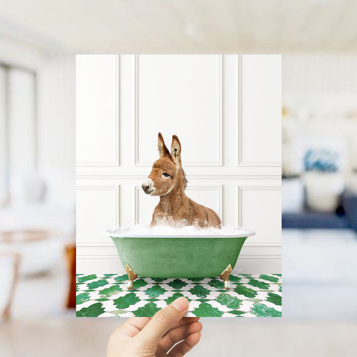 A donkey is sitting in a green bathtub filled with bubbles, with a person's hand holding the image up to the camera.